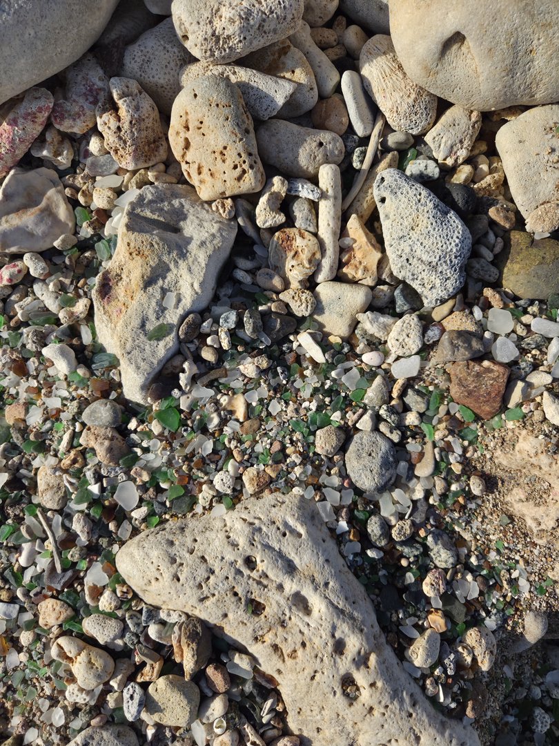 Drifts of small green and white sea glass packed into the gaps between pale coral boulders